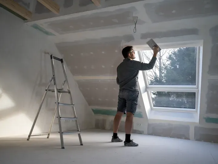 Plasterer skimming a sloped ceiling beside a roof window